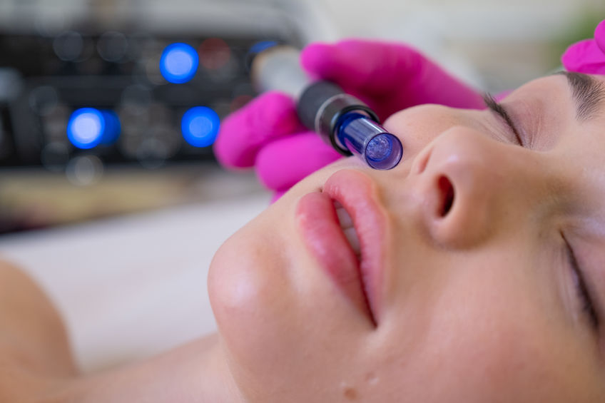 Woman in a spa salon on cosmetic procedures for facial care. Beautician makes skin care procedure on a face. Cosmetologist making a woman a therapeutic laser processing on a face.